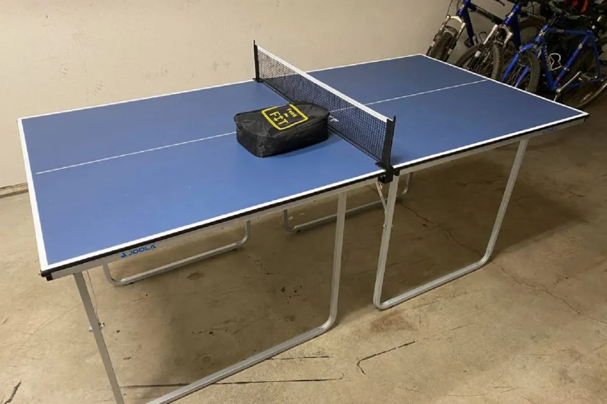 A well-lit game area featuring a ping pong table with a net set up, and a black sports bag resting nearby. The space feels lively and inviting for friendly competition or relaxed socializing.