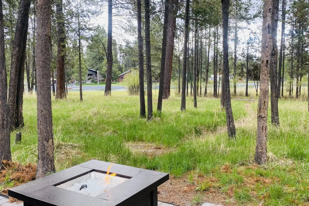 A cozy fire pit is set in an open, grassy area surrounded by mature trees, offering a space for outdoor gatherings, relaxation, and connection with nature. The setting is ideal for stargazing or sharing stories after a day of work or adventure.