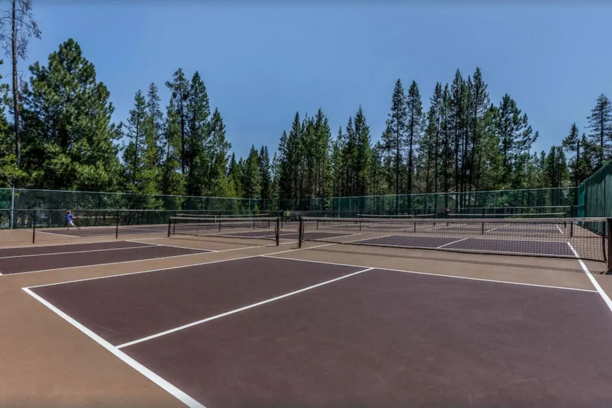 A set of tennis courts nestled among tall trees, with active players on the courts, creating a lively scene of recreation and social connection amidst nature.