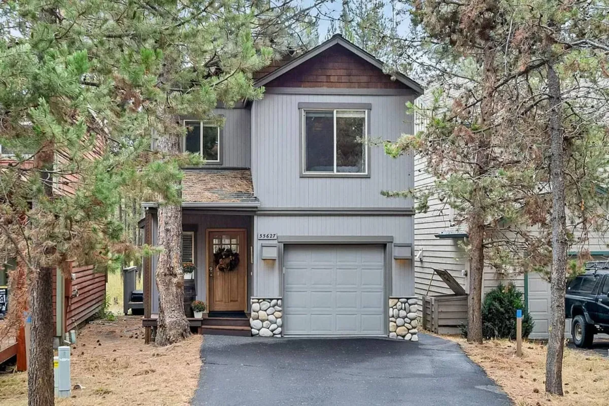 The image features the welcoming exterior of a charming single-family house surrounded by lush landscaping and tall trees. The front door is adorned with holiday decorations, adding a festive, homey touch, while the spacious front yard invites outdoor play, family gatherings, and summer barbecues.