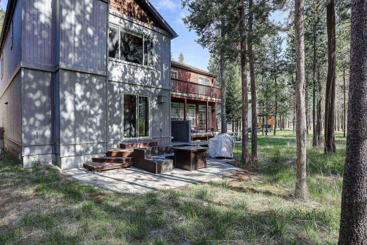 A view of the deck connected to the house, with outdoor seating and lush trees providing a backdrop. The space is set up for outdoor dining and relaxation, inviting guests to enjoy sunsets and tranquil evenings.