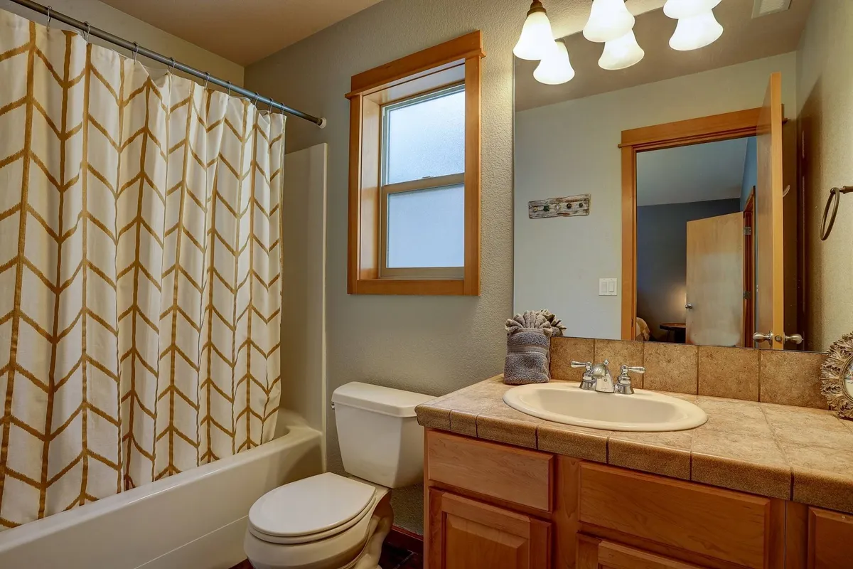 A calm, bright bathroom with a modern vanity, shower curtain, window allowing sunlight, and a large mirror. The space feels fresh and inviting, ideal for self-care and relaxation.