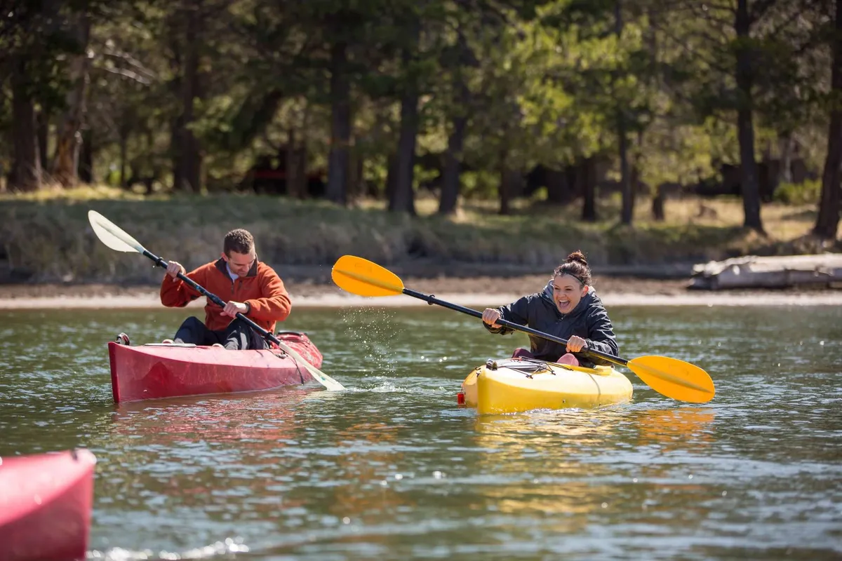 This image features two kayakers gliding over vibrant waters, surrounded by lush trees in the background. The scene is energetic and joyful, capturing the excitement of river activities available in the area.