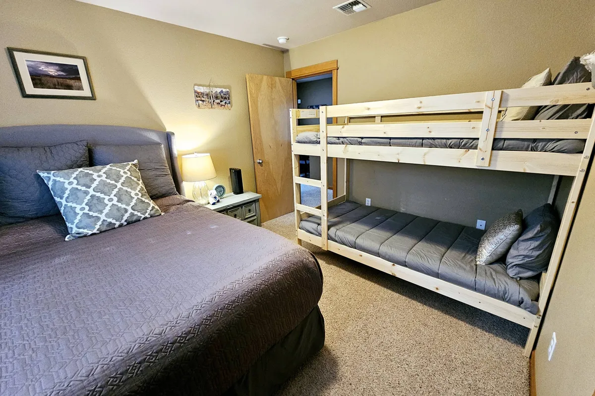 A bright and comfortable bedroom with a queen bed and a twin bunk bed, complemented by a lamp and decorative pillows. The setup caters to families or groups, offering both coziness and flexibility.