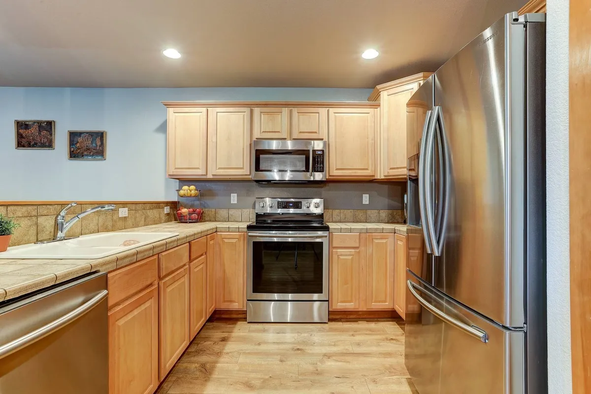 A bright and welcoming kitchen featuring modern stainless steel appliances, light wood cabinetry, and a spacious kitchen island. The layout suggests space for group meal prep and casual conversation.