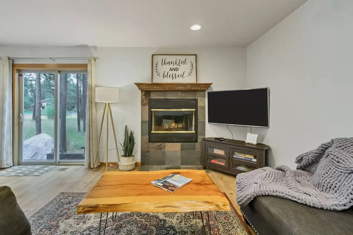 This interior image centers on the living room, showcasing a plush sofa, a coffee table, a gas fireplace, and a flat-screen TV. The warm ambiance and seating arrangement highlight the communal aspect of the home, perfect for gatherings and movie nights.