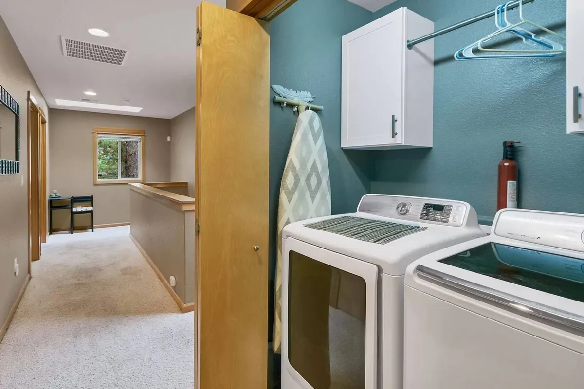 A practical laundry room with a full-size washer and dryer beside a sunlit window and organized shelving. The space is clean and functional, making post-adventure chores seem convenient and accessible.